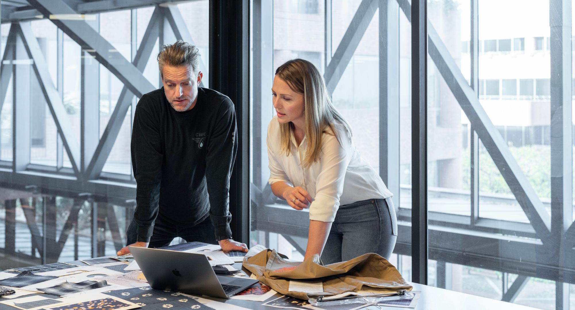 homem e mulher apoiados numa mesa olhando algo na tela do notebook