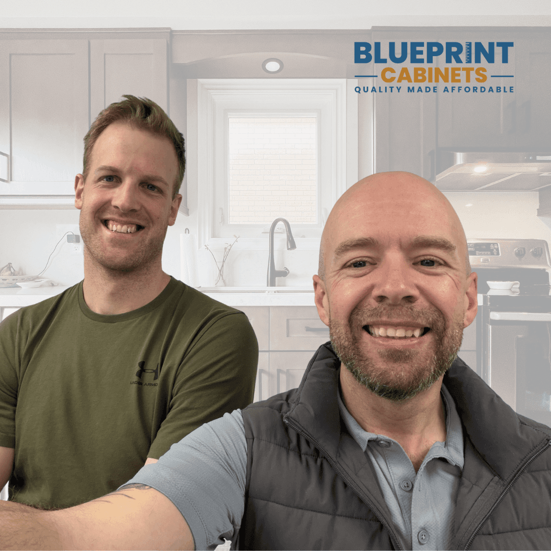 Two BluePrint Cabinets founders smiling in modern kitchen showroom with company logo displayed overhead.