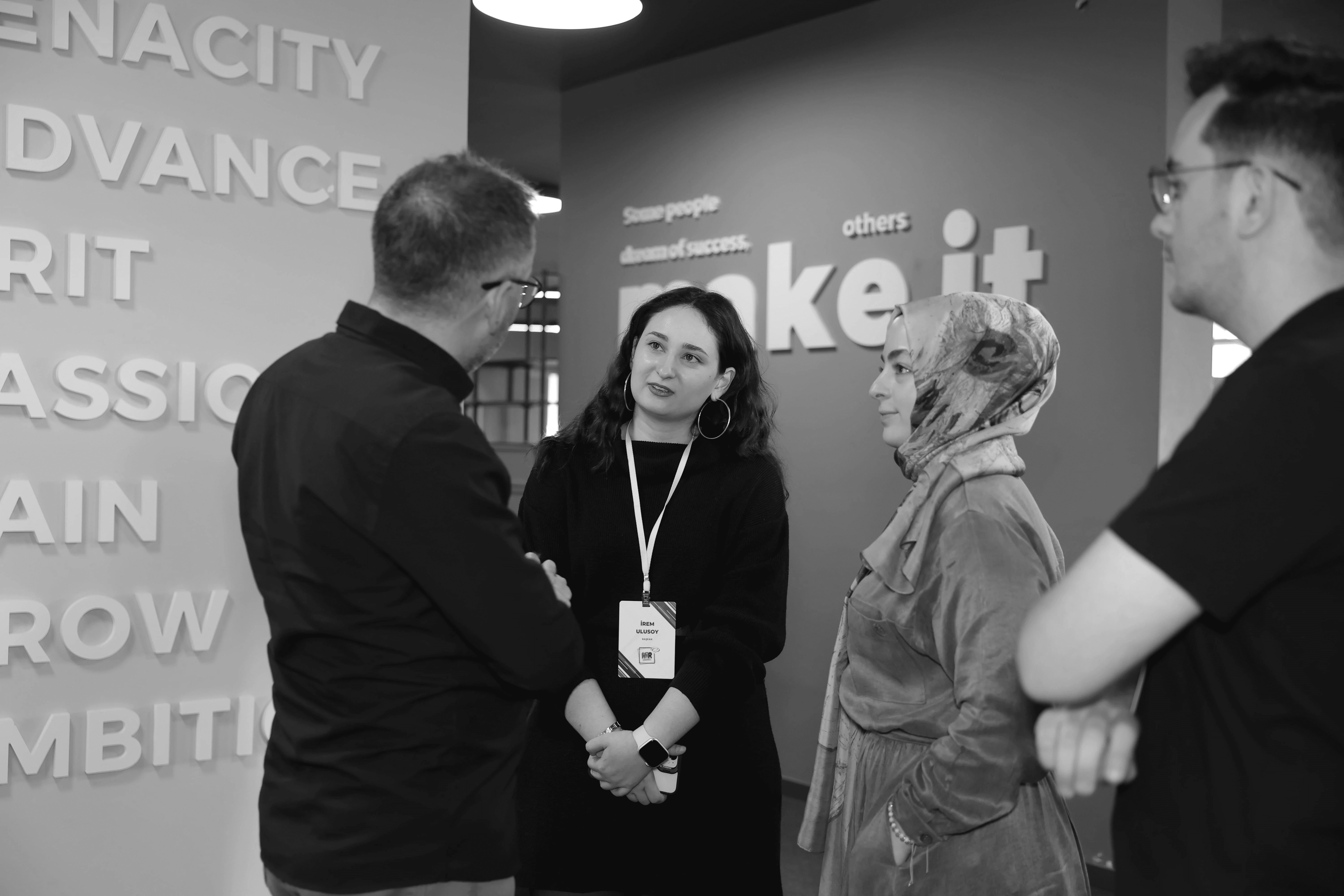 Four people engage in conversation in front of a wall with text, all smiling and interacting in a casual setting.