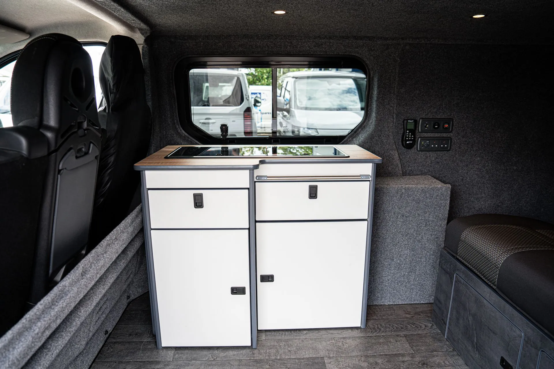 Compact white kitchen pod with an oak-effect worktop and glass-lidded hob and sink beneath an opening side window