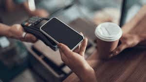 Eine Kundin hält ihr Smartphone an ein Kartenterminal, um einen Kaffee zu bezahlen – der Wandel von Bargeld zu kontaktlosem Bezahlen.