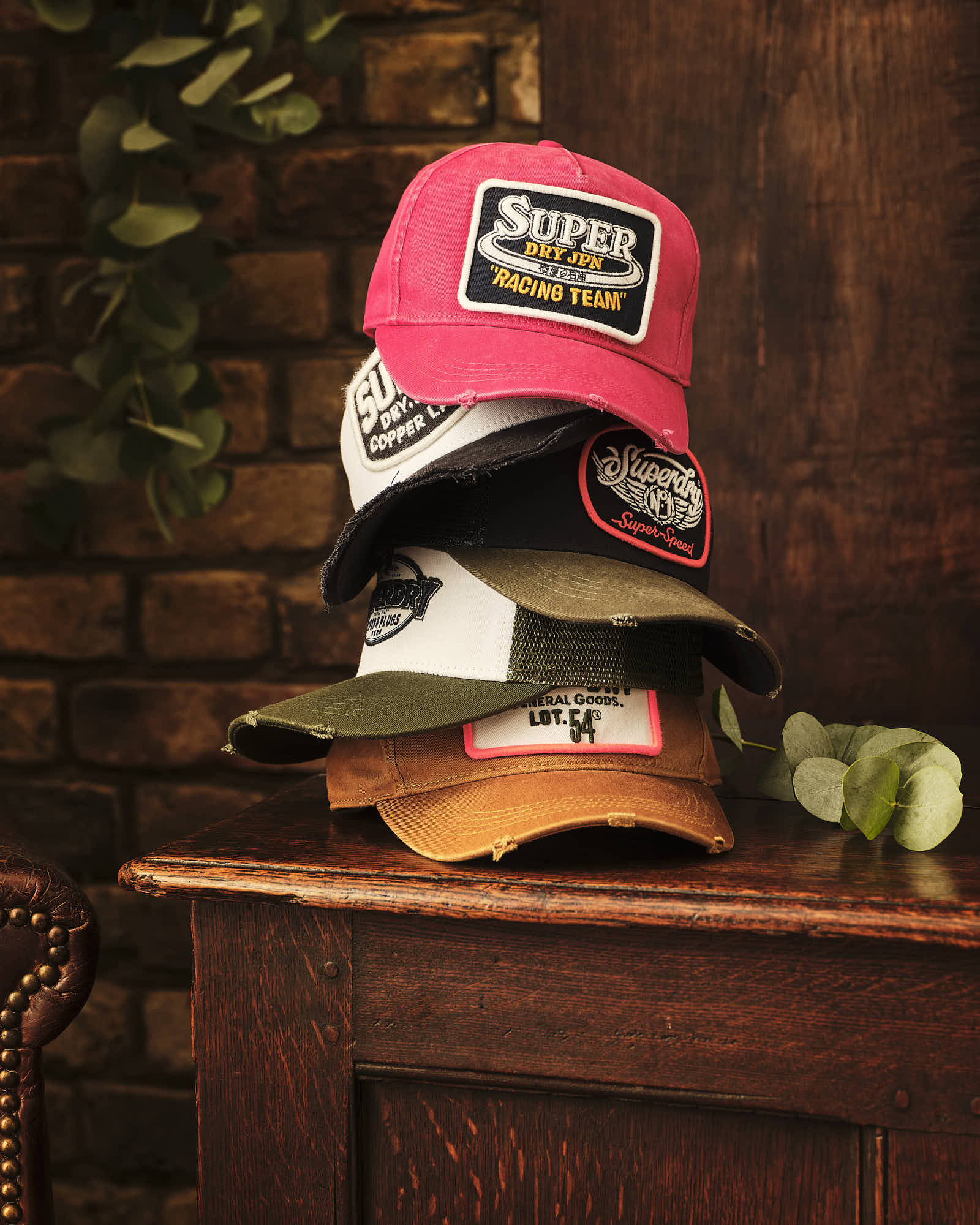 Stack of colorful branded caps on wooden table with brick wall background.