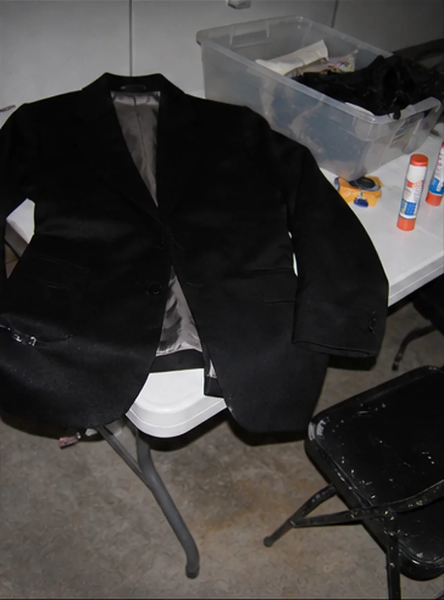 Direct-flash studio photograph of a black suit, candy wrappers, hot glue, and hand tools during the first construction.