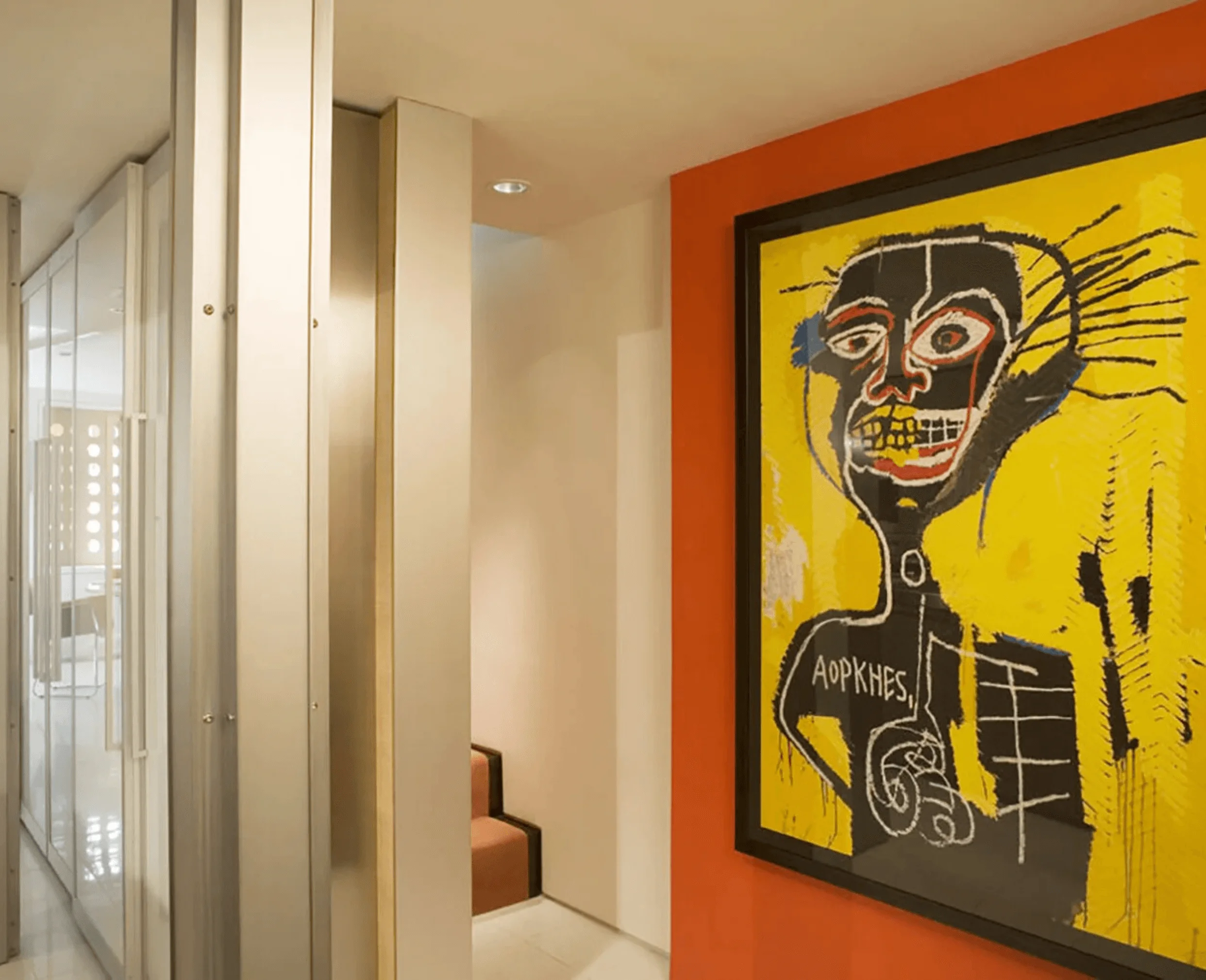 A mirrored hallway leads toward a stairwell, with a large Basquiat-inspired painting hung on an orange accent wall