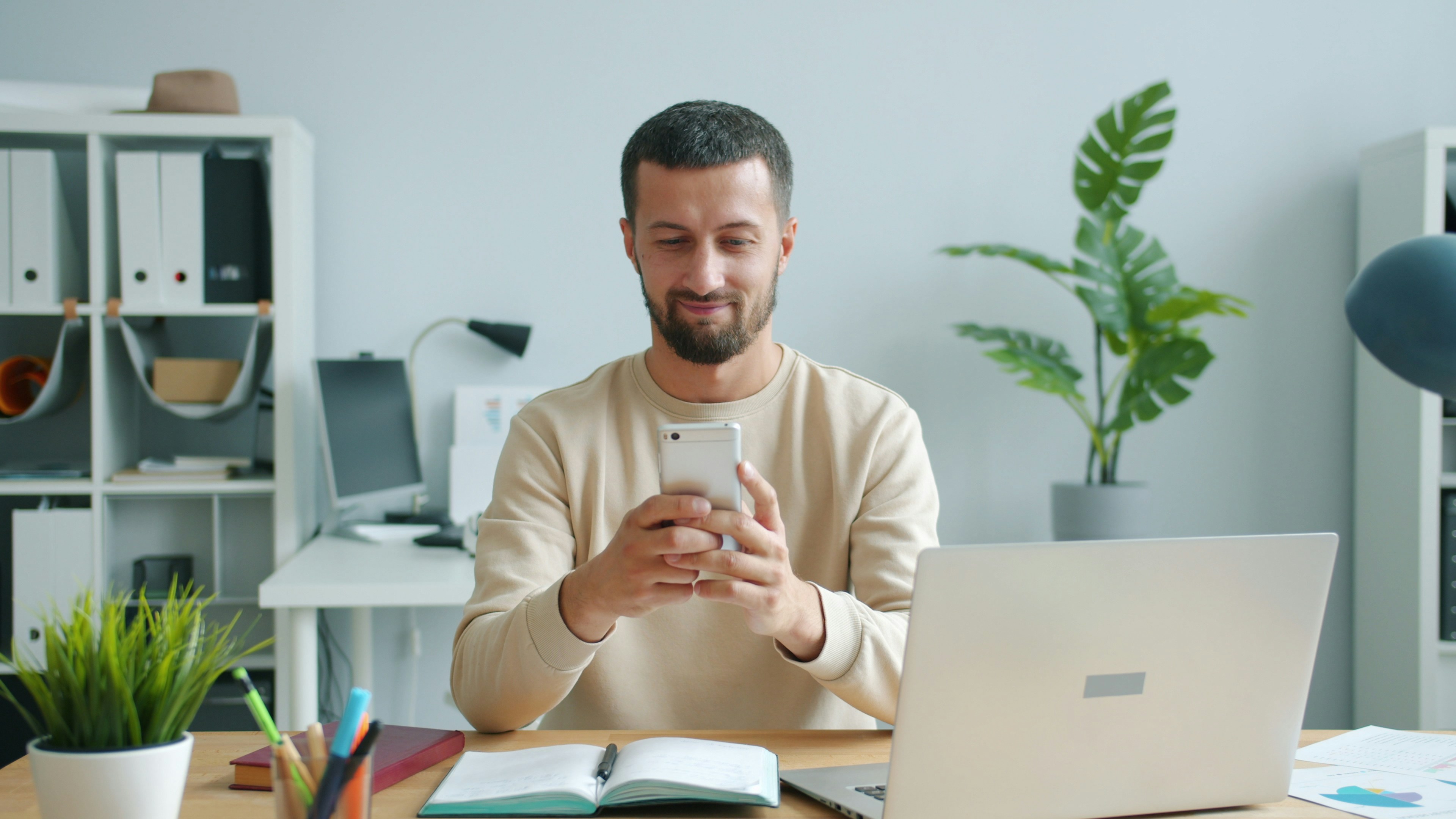 Carefree middle-aged man is using smartphone smiling working in office at work enjoying communication