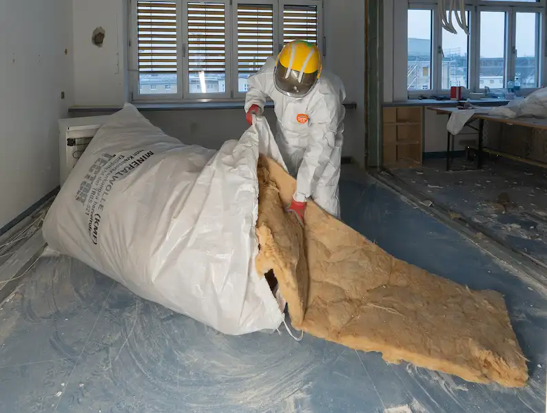 Arbeiter in Schutzanzug bei Schadstoffsanierung beim Verpacken von Mineralwolle in Entsorgungssack im Innenbereich