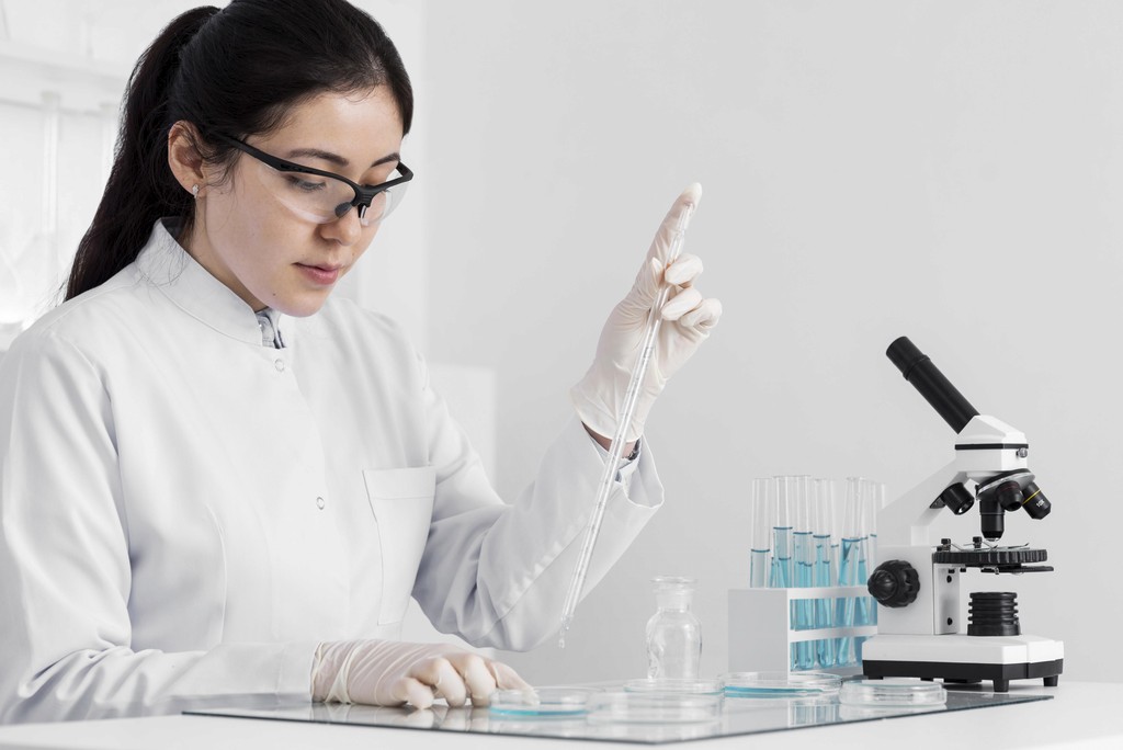 A woman in a lab coat intently examines a computer screen in a laboratory setting.