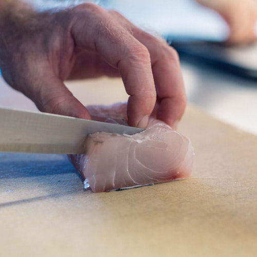 一只手在切菜板上用刀切一块生鱼片。