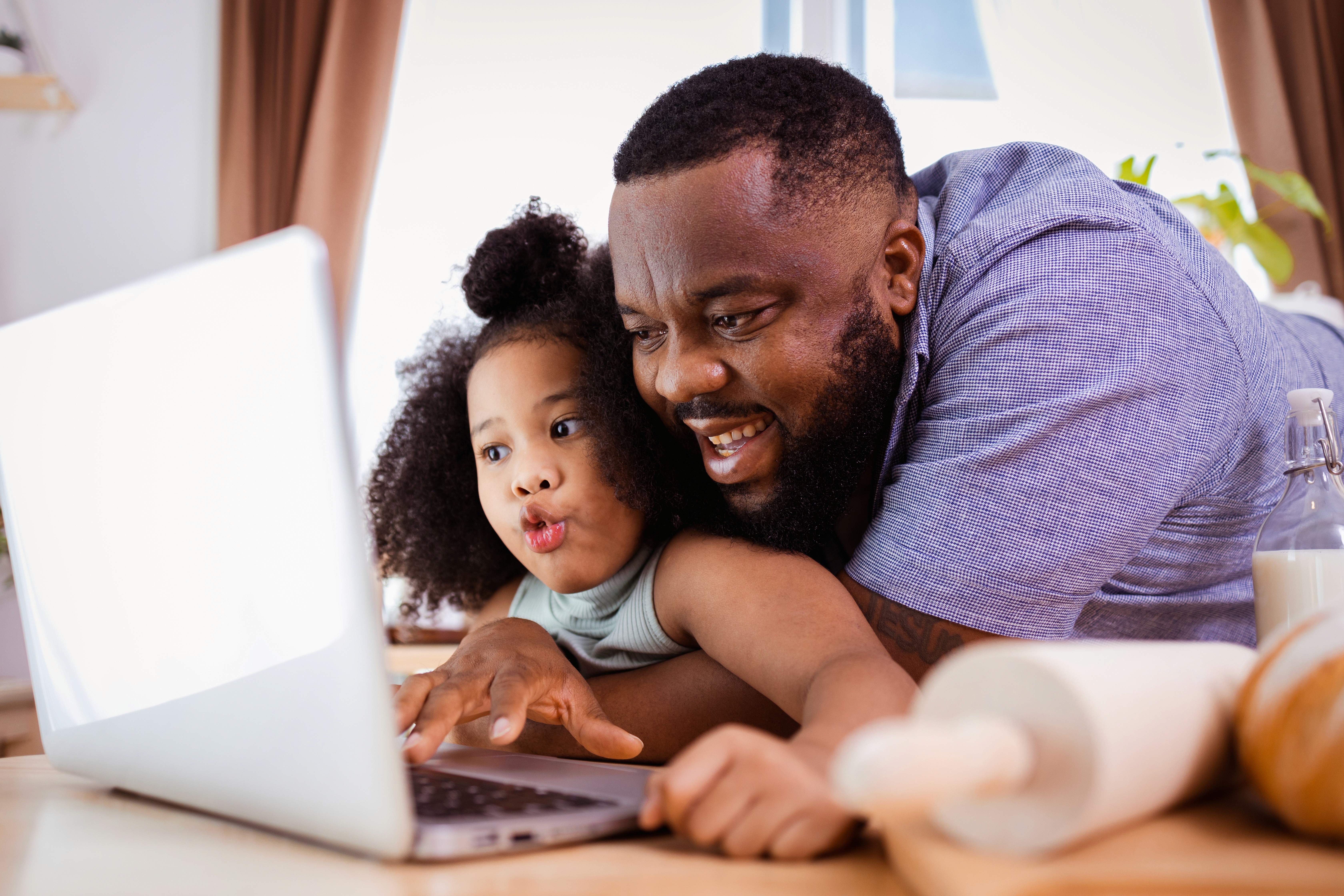 Father smiling at a laptop with his young daughter leaning over his shoulder, representing how a new child or remarriage can affect child support and alimony modifications in Massachusetts