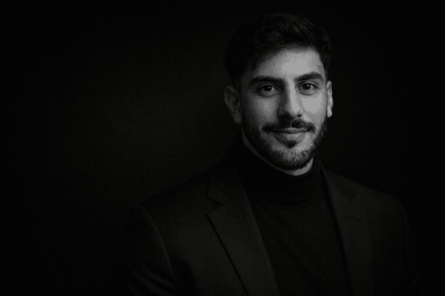 Portrait of product designer Peter Szabo in a black turtleneck and blazer against a dark background.