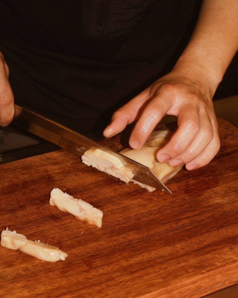 A person slicing a piece of food on a wooden cutting board with a sharp knife.