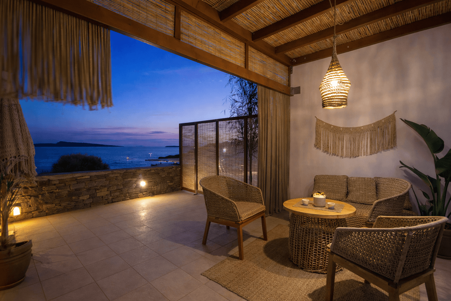 Outdoor patio with rattan furniture, a woven pendant light, and a scenic view of the water at dusk.