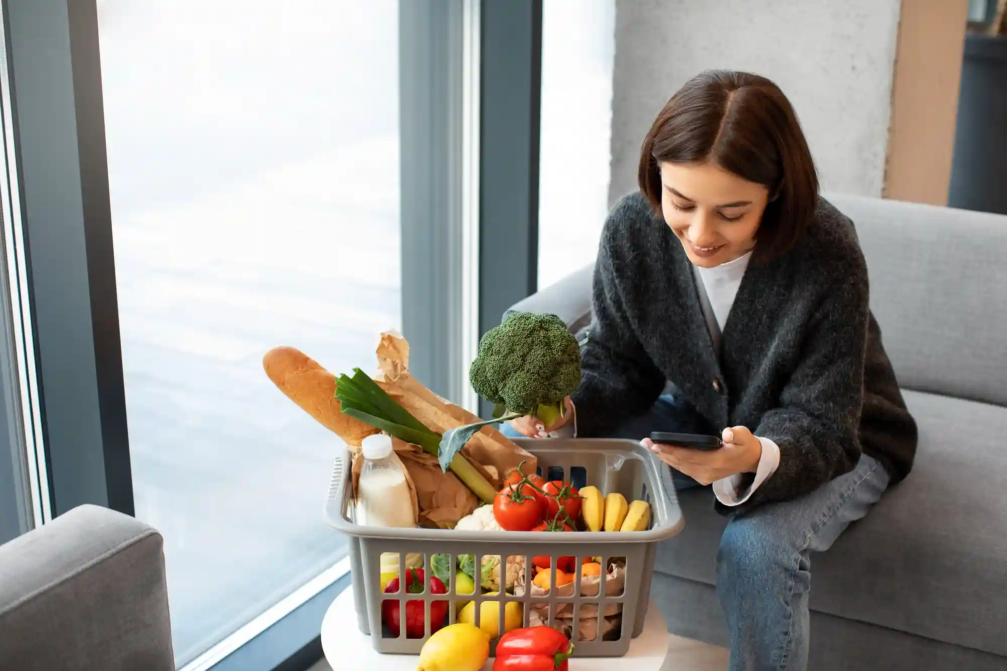 A smiling woman sitting on a sofa while using her smartphone to order fresh groceries for home delivery.