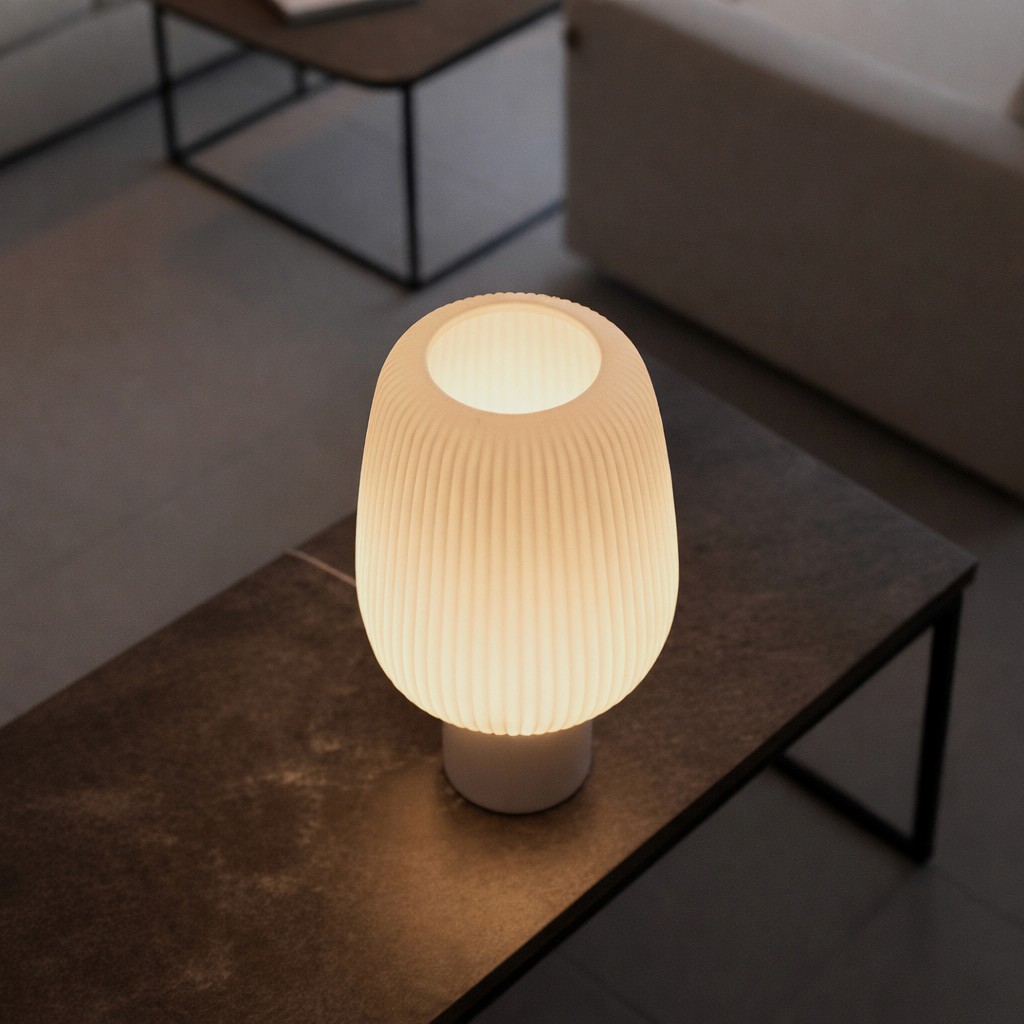 Glowing ribbed table lamp on a dark table, high-angle view showing the open top.