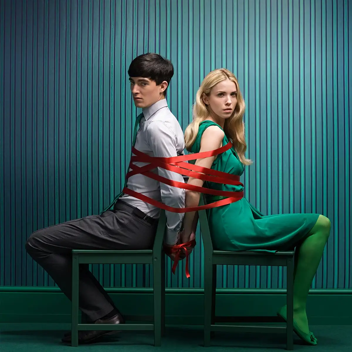 Two people seated back to back, bound together with red tape, symbolising organisational tension, constraint, and resistance to change.