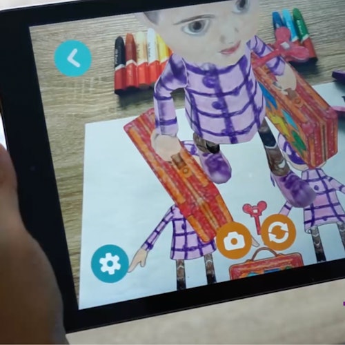 A tablet displaying an augmented reality figure of a child holding suitcases, over a paper drawing, with markers in the background.