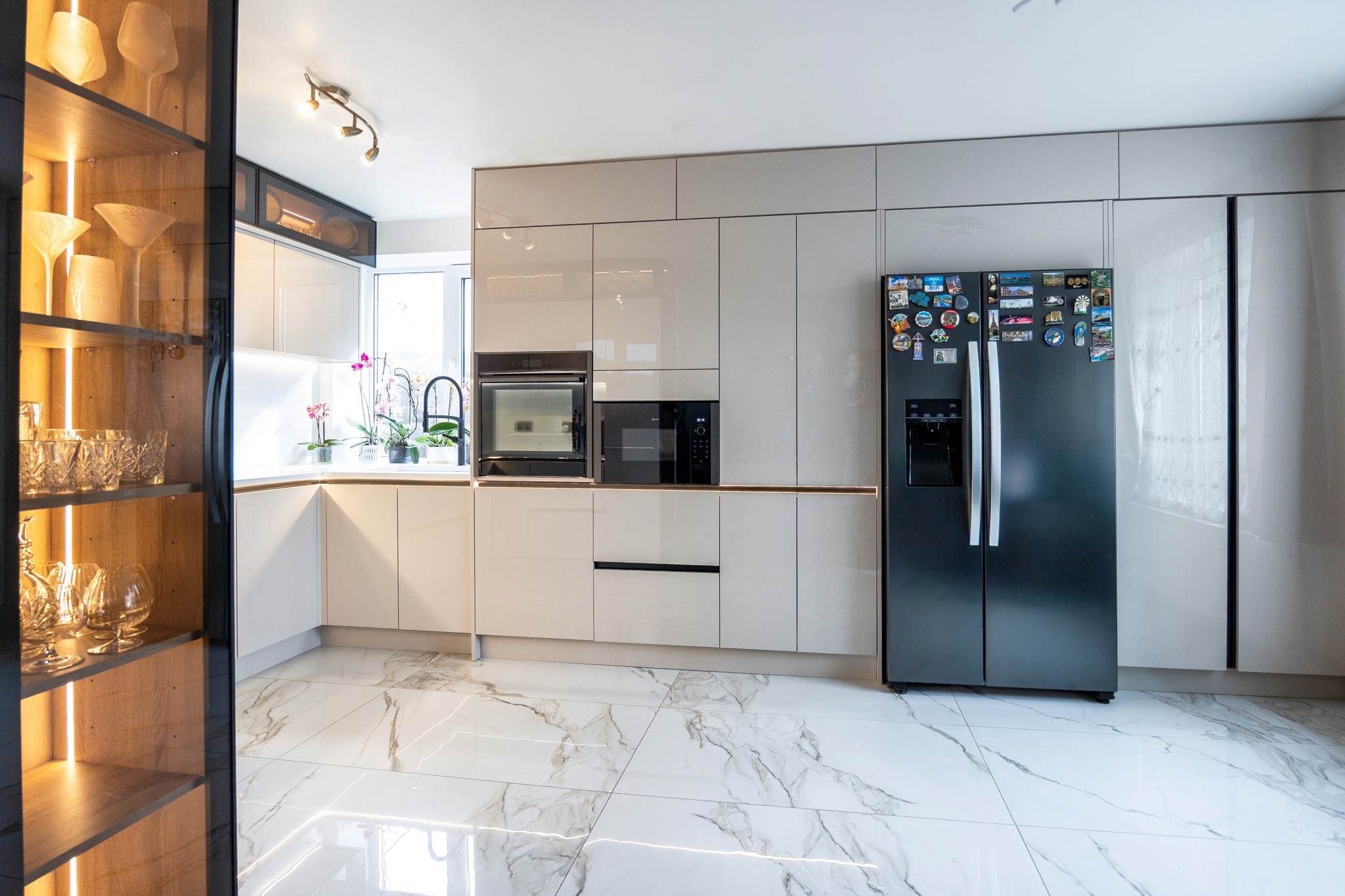 Modern two-story home with large glass windows, warmly lit interiors, and a balcony. Surrounded by trees and a manicured lawn at dusk. Cozy ambiance.