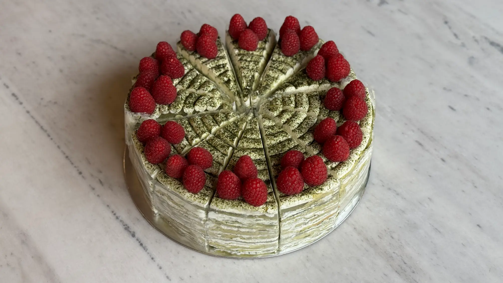 Green matcha layer cake with fresh raspberries and pistachio decoration in fan pattern