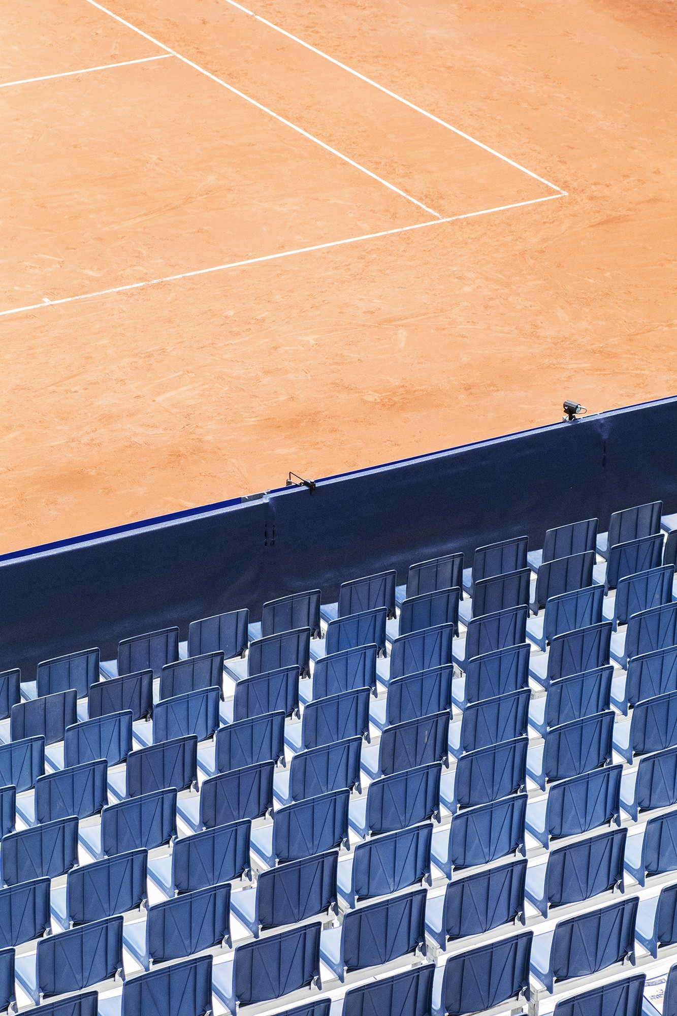 Détail d'un court de tennis avec les gradins bleus en premier plan qui sont vides