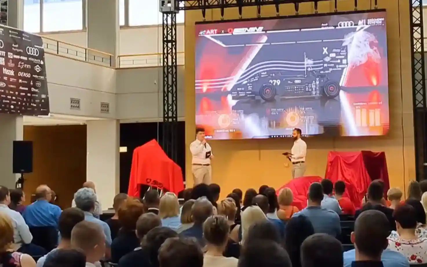 Publik på ett Audi-evenemang som ser en 3D-animation av en tävlingsbil på storbild
