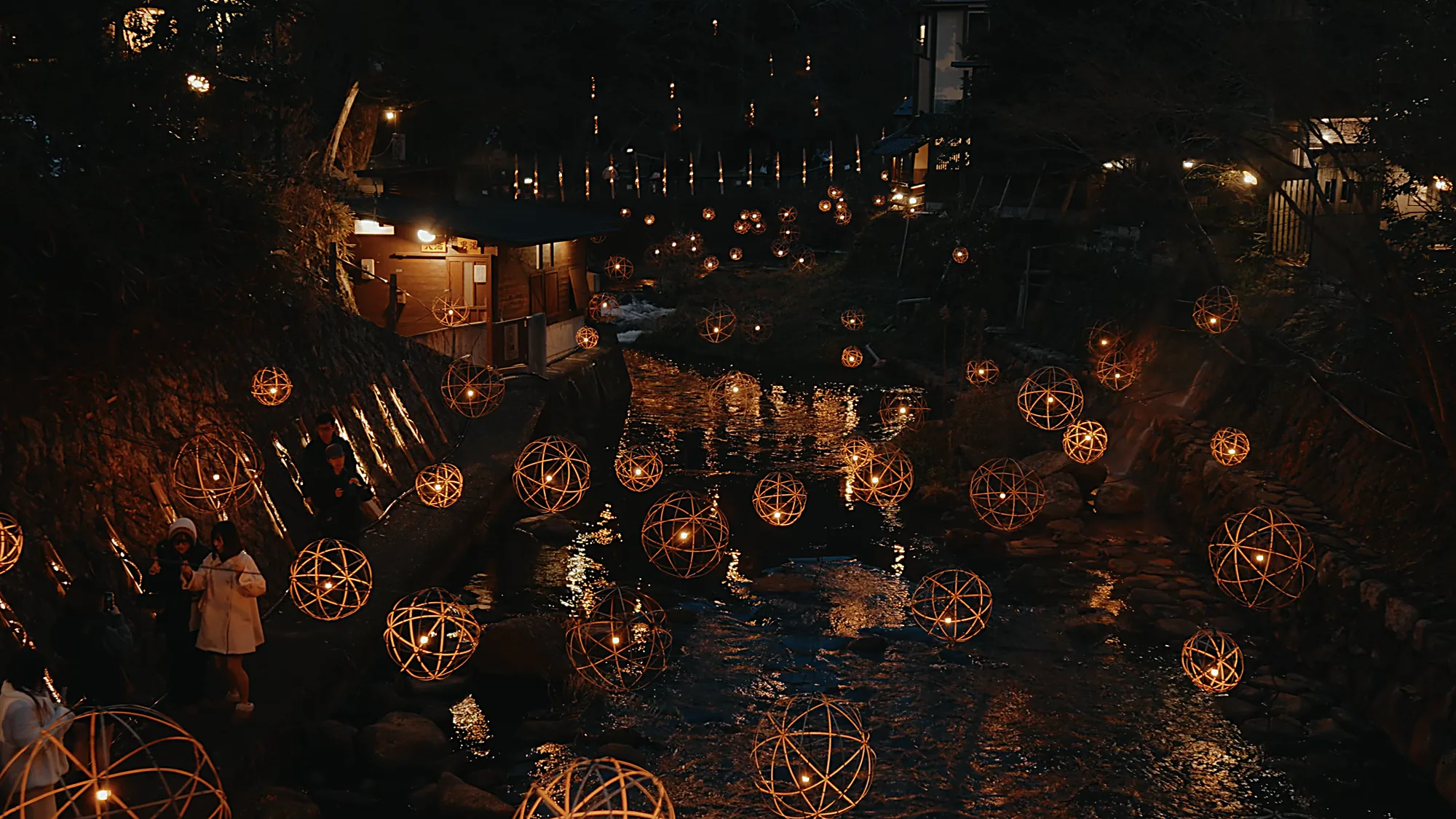 Lantern spheres massed on the river during Yuakari at Kurokawa Onsen, figures on the bank