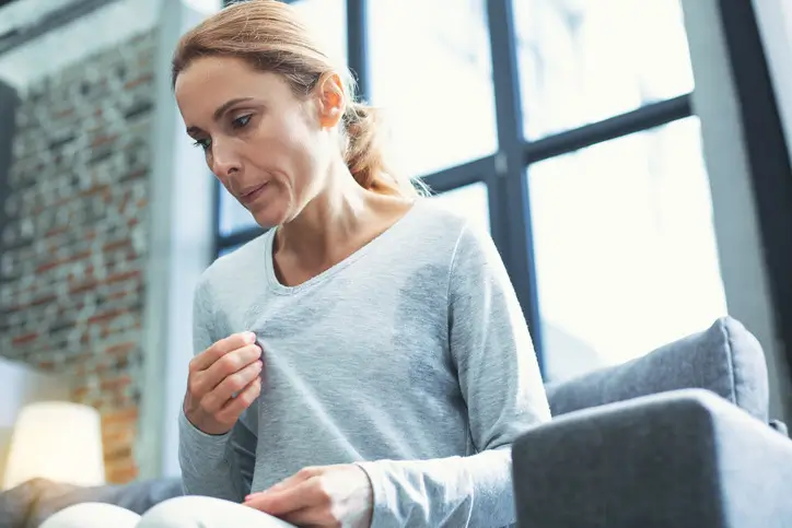 Woman with sweat patches on shirt feeling hot, menopause hot flashes concept