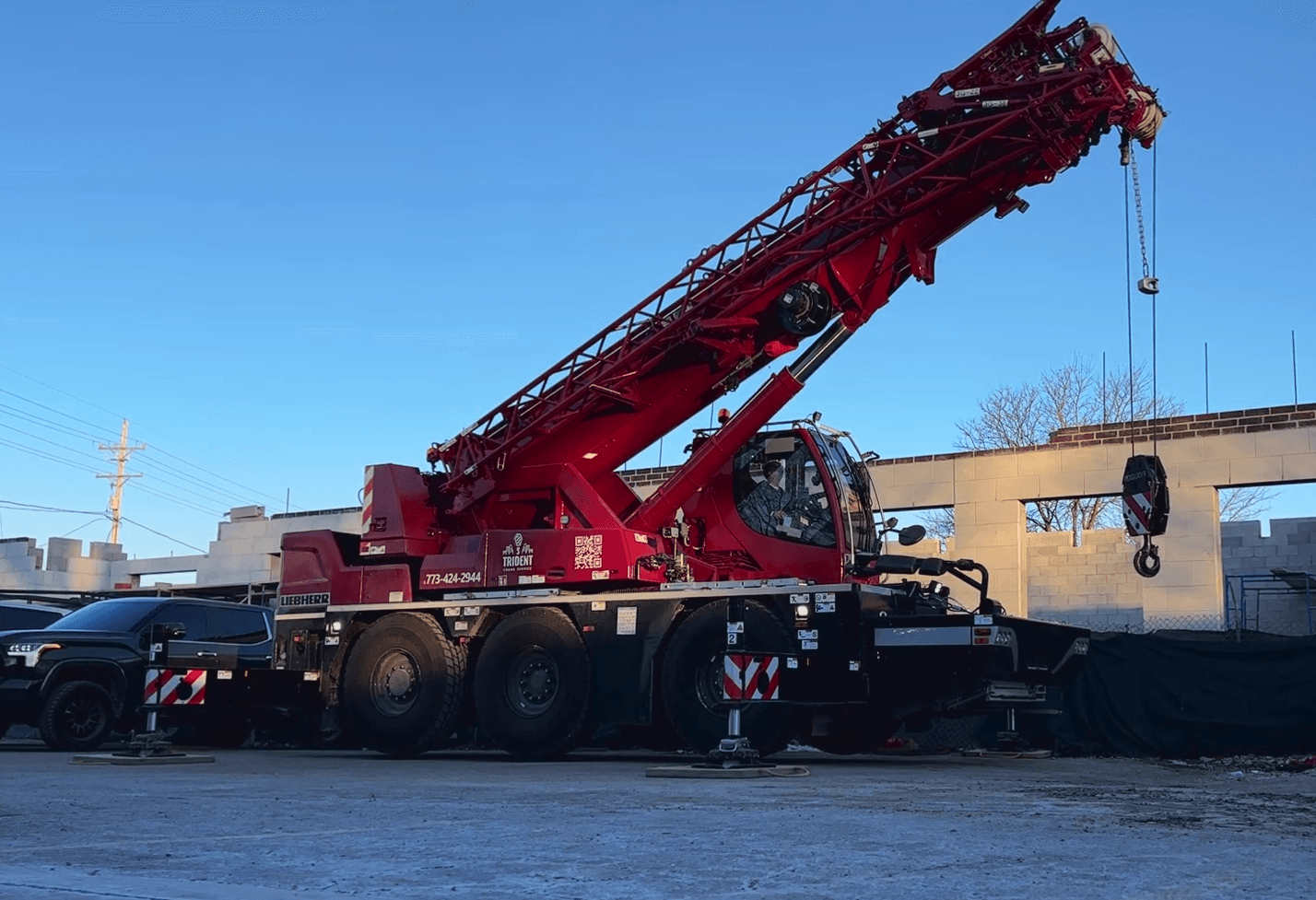A large red crane truck is parked on a construction site, with its boom extended upward against a clear blue sky.