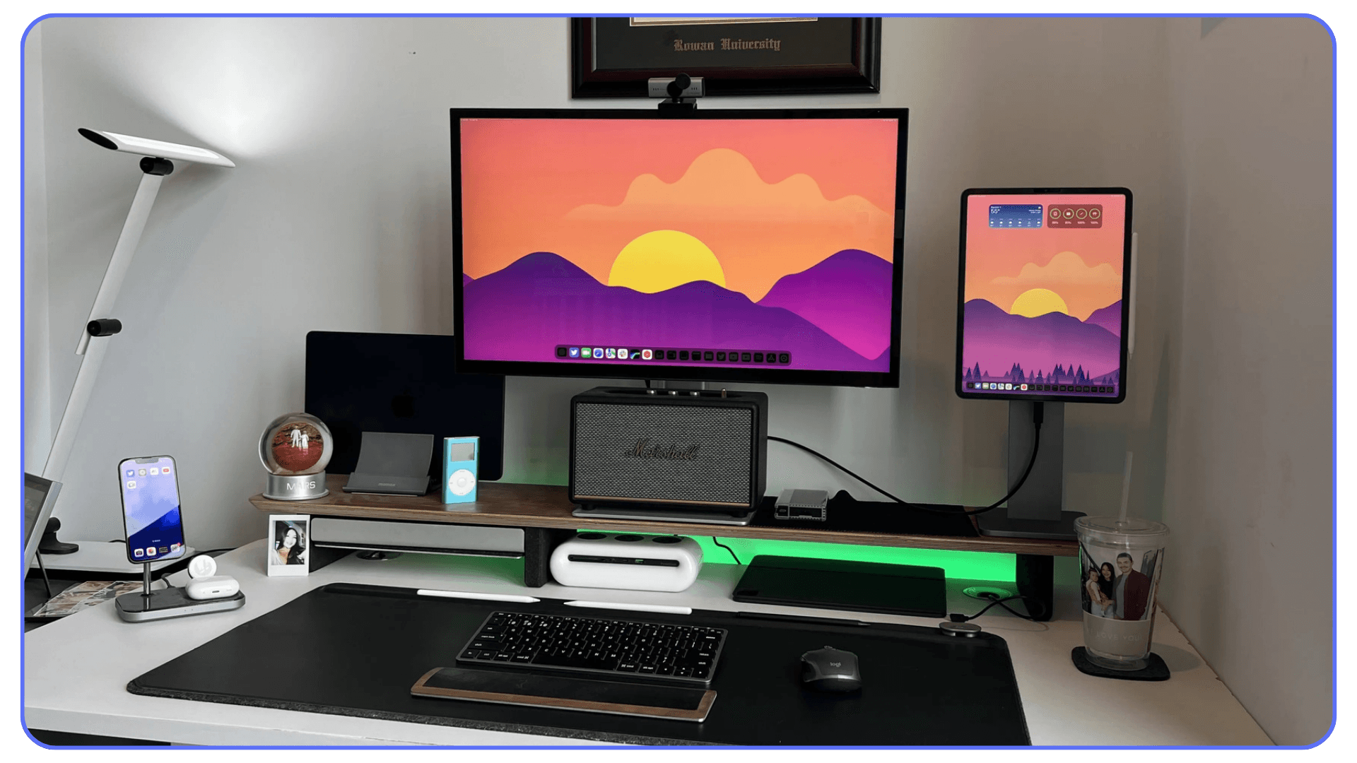 Modern home office setup with monitor, iPad, iPhone, keyboard, and speakers on a minimalist white desk.