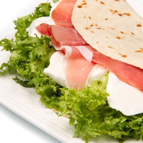 Close-up of a flatbread wrap with prosciutto, mozzarella cheese, and leafy lettuce on a white plate.
