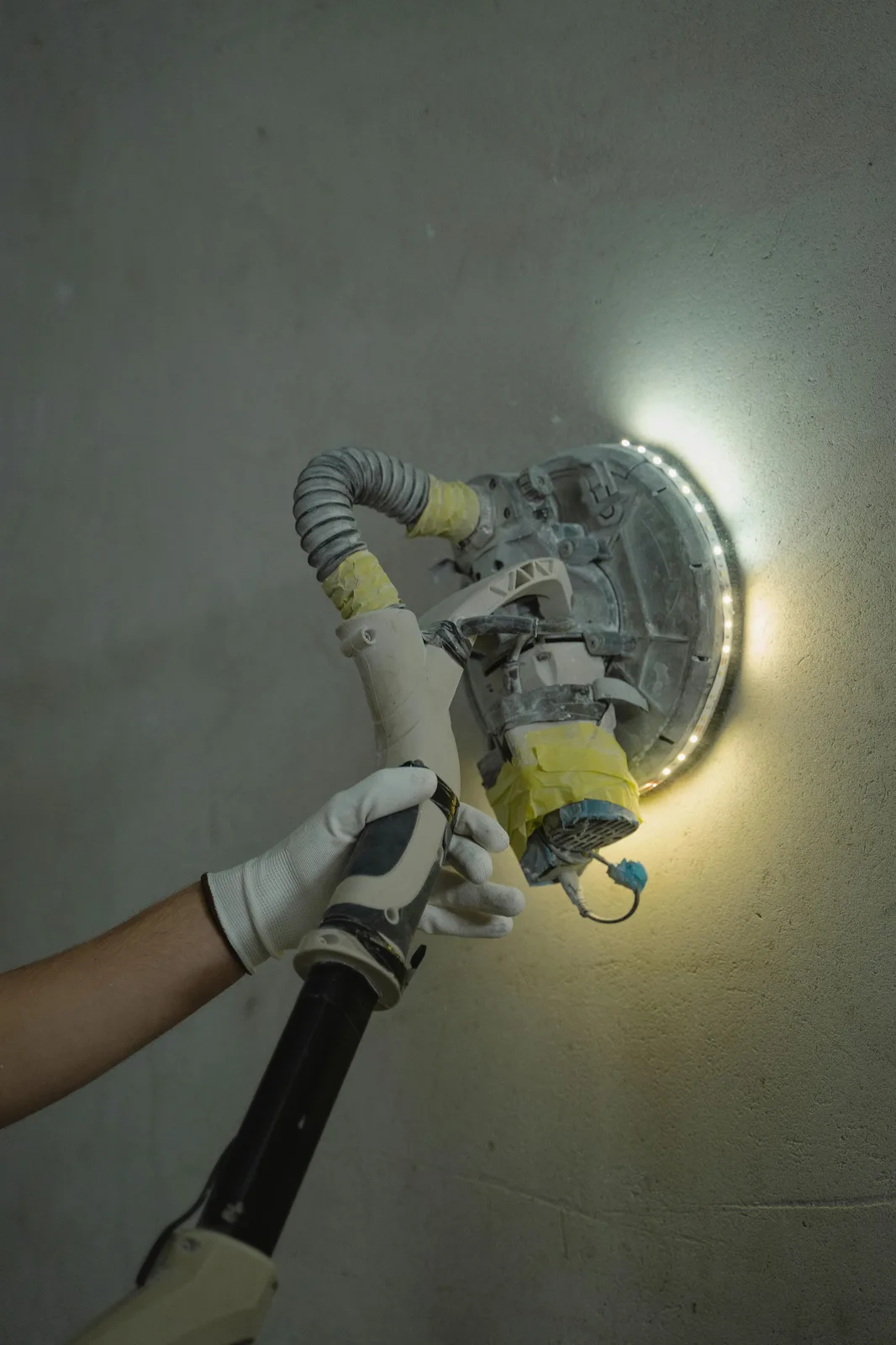 Worker using illuminated drywall sander on wall surface