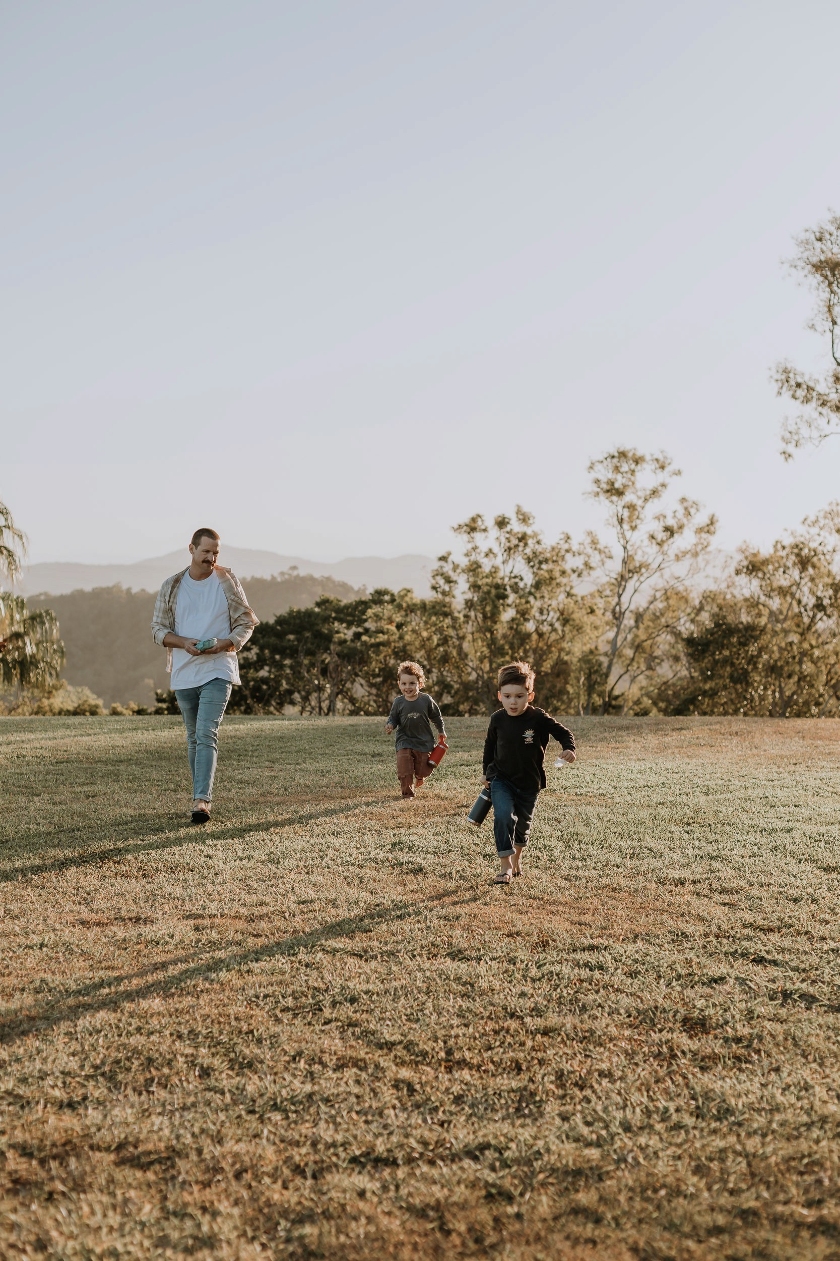 Candid family moment during a sunset photo session in an open grassy field, parent and children running.