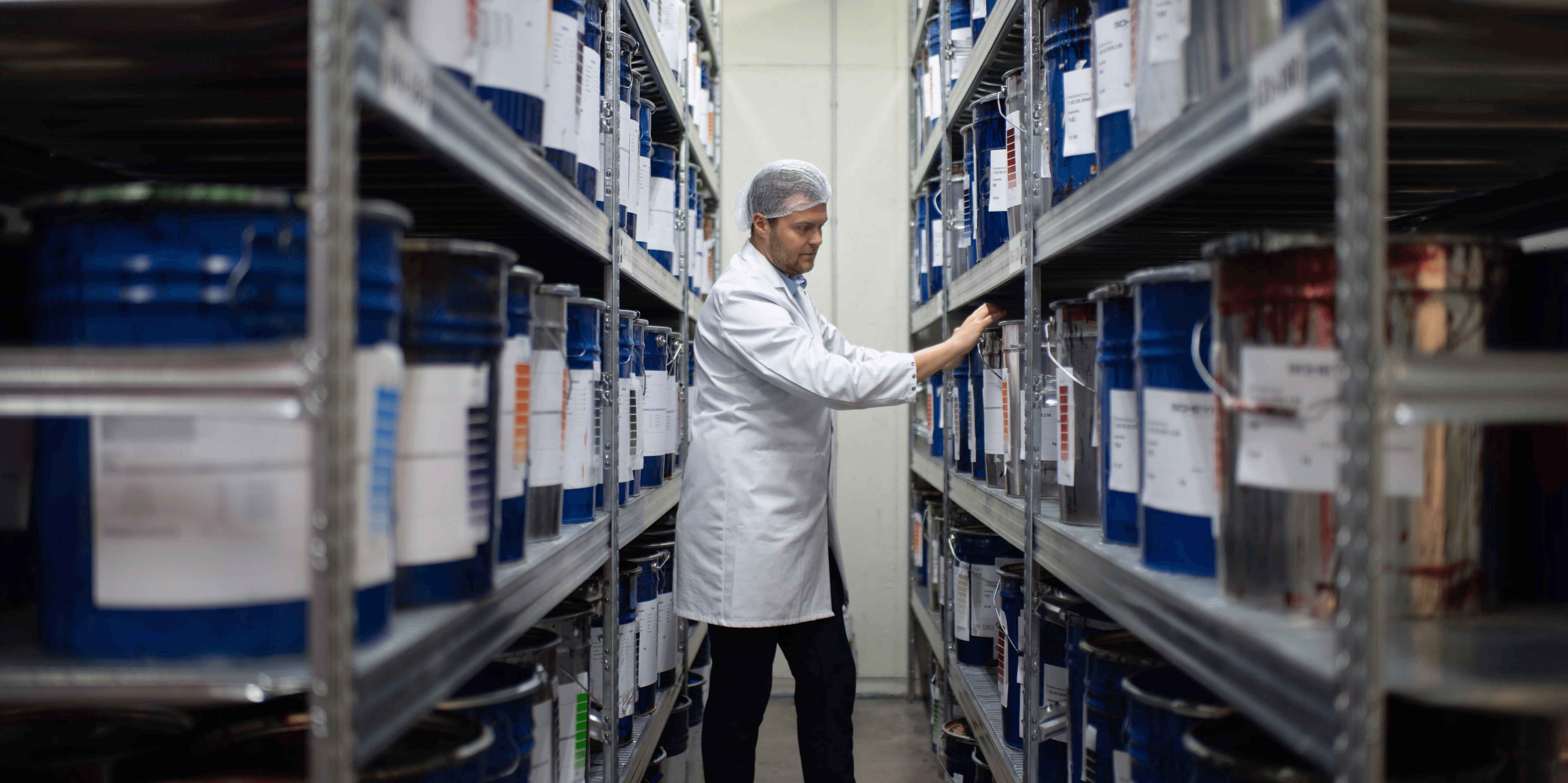 Scheyer employee wearing a lab coat examining containers stored in a warehouse aisle.