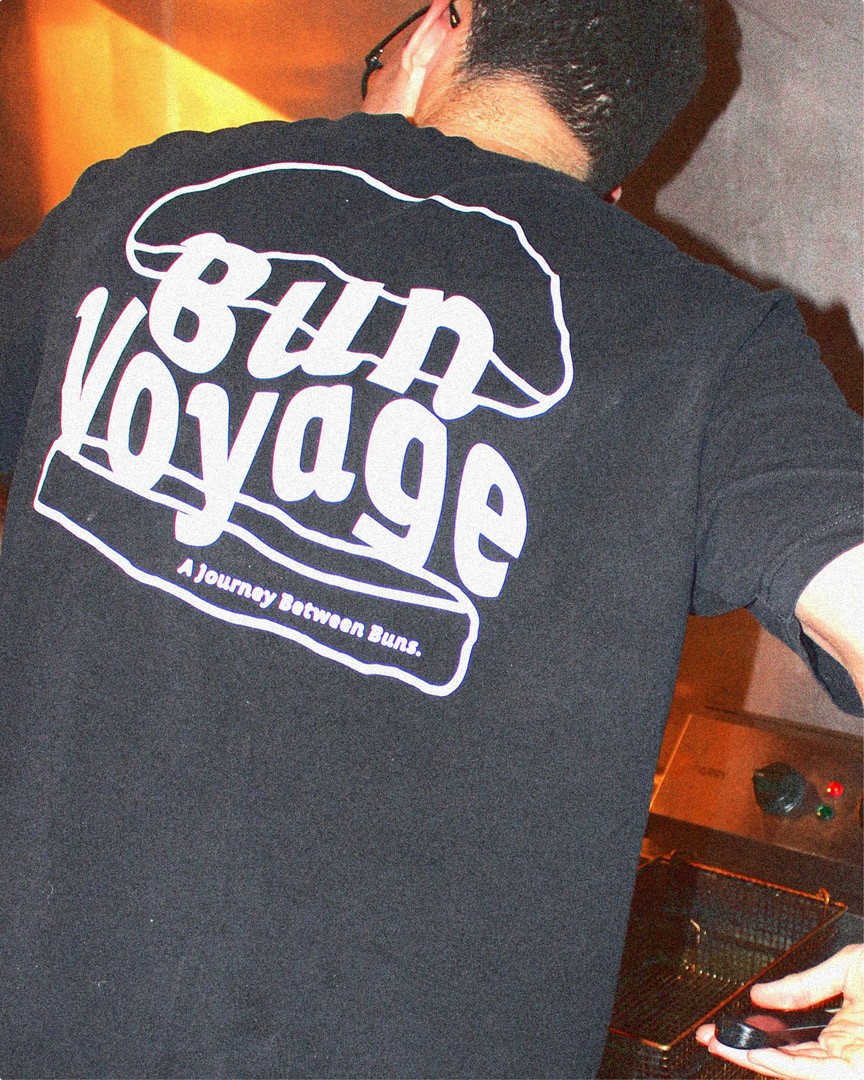 Bun Voyage branding on the back of a black t-shirt of a man cooking in the kitchen
