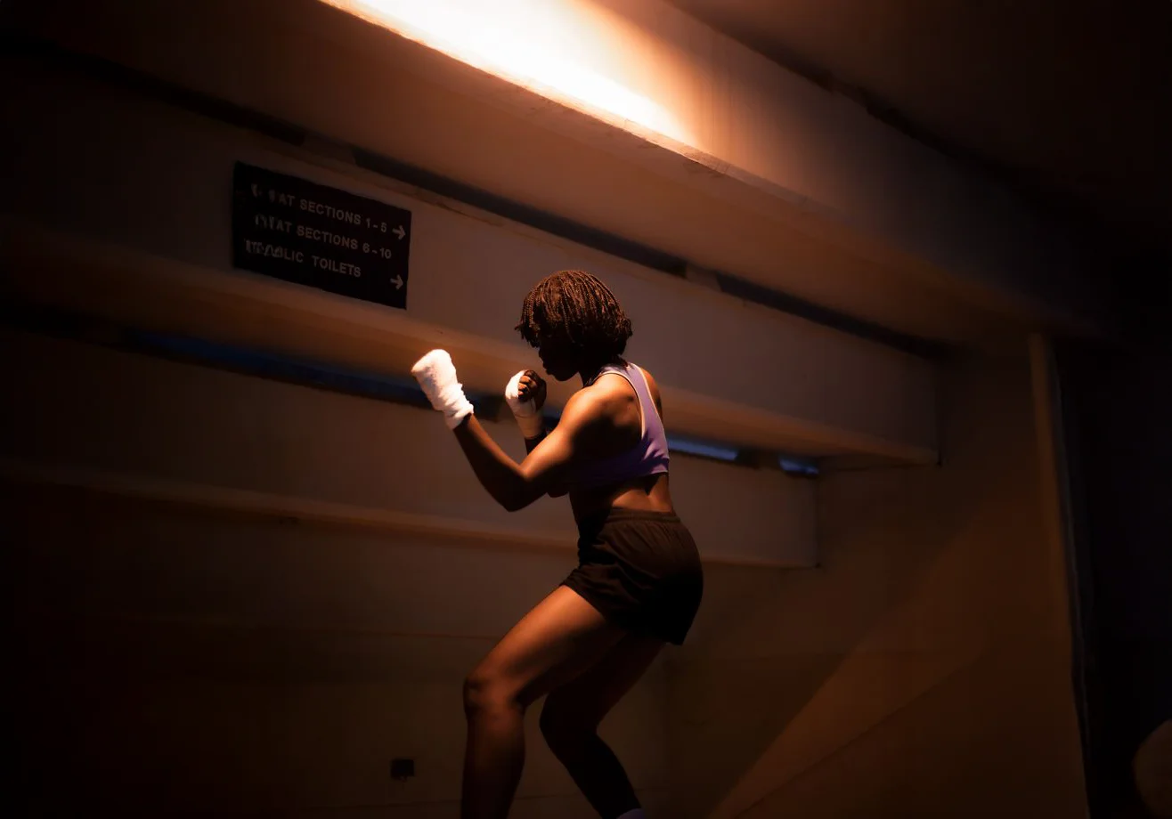 Woman in a boxing stance with hand wraps under dramatic lighting.