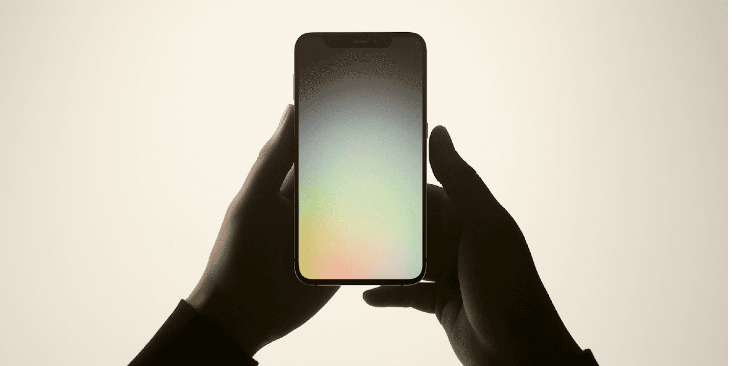 Hands holding a smartphone with a soft multicolor gradient screen.