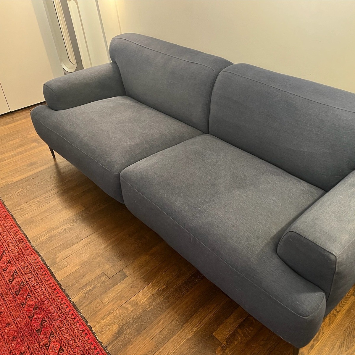 Dark gray Abisko sofa with a simple, clean design on a wooden floor and a red area rug