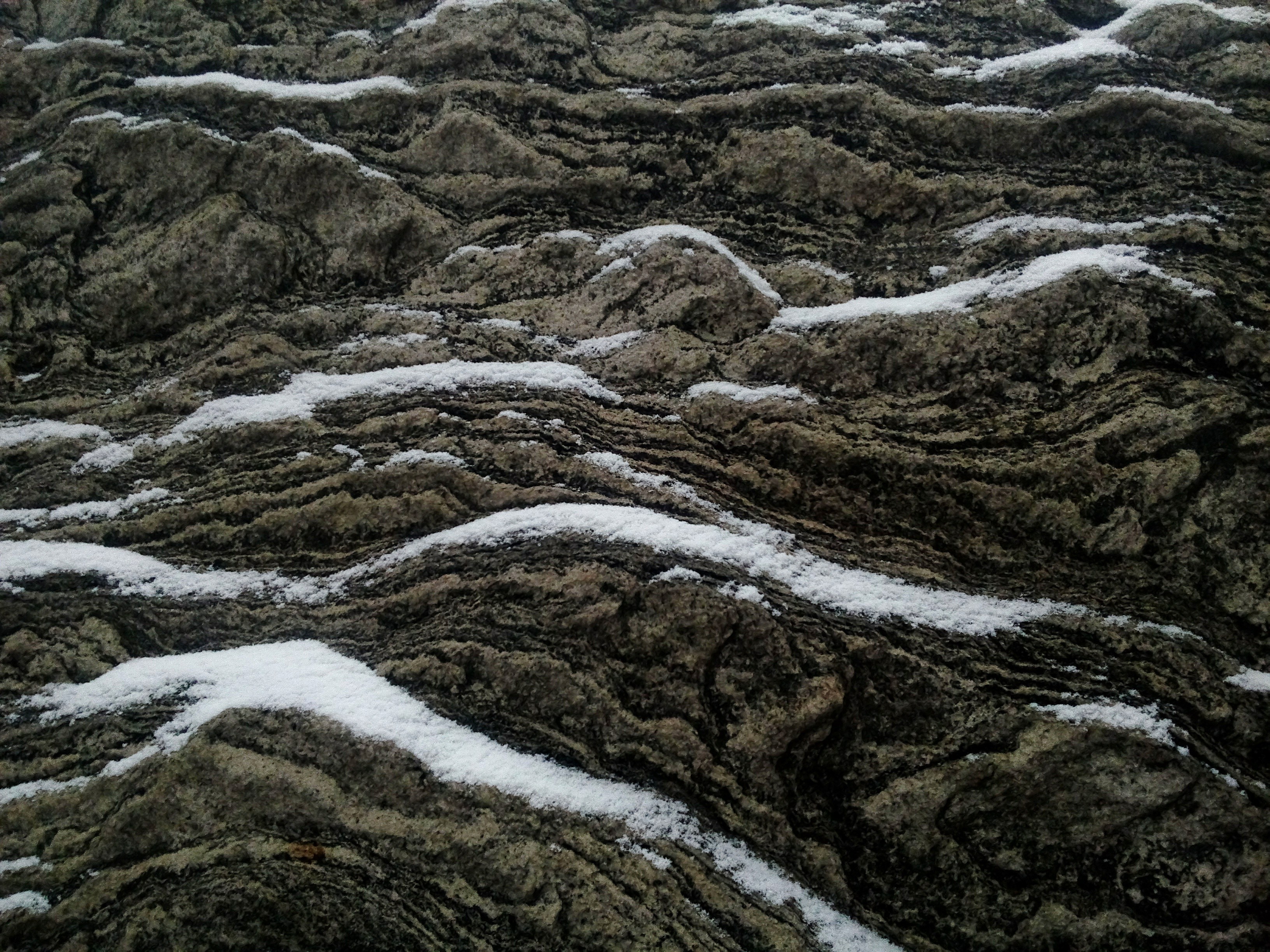 A close-up of textured rocks with wavy patterns, featuring patches of white water flowing over the surface.