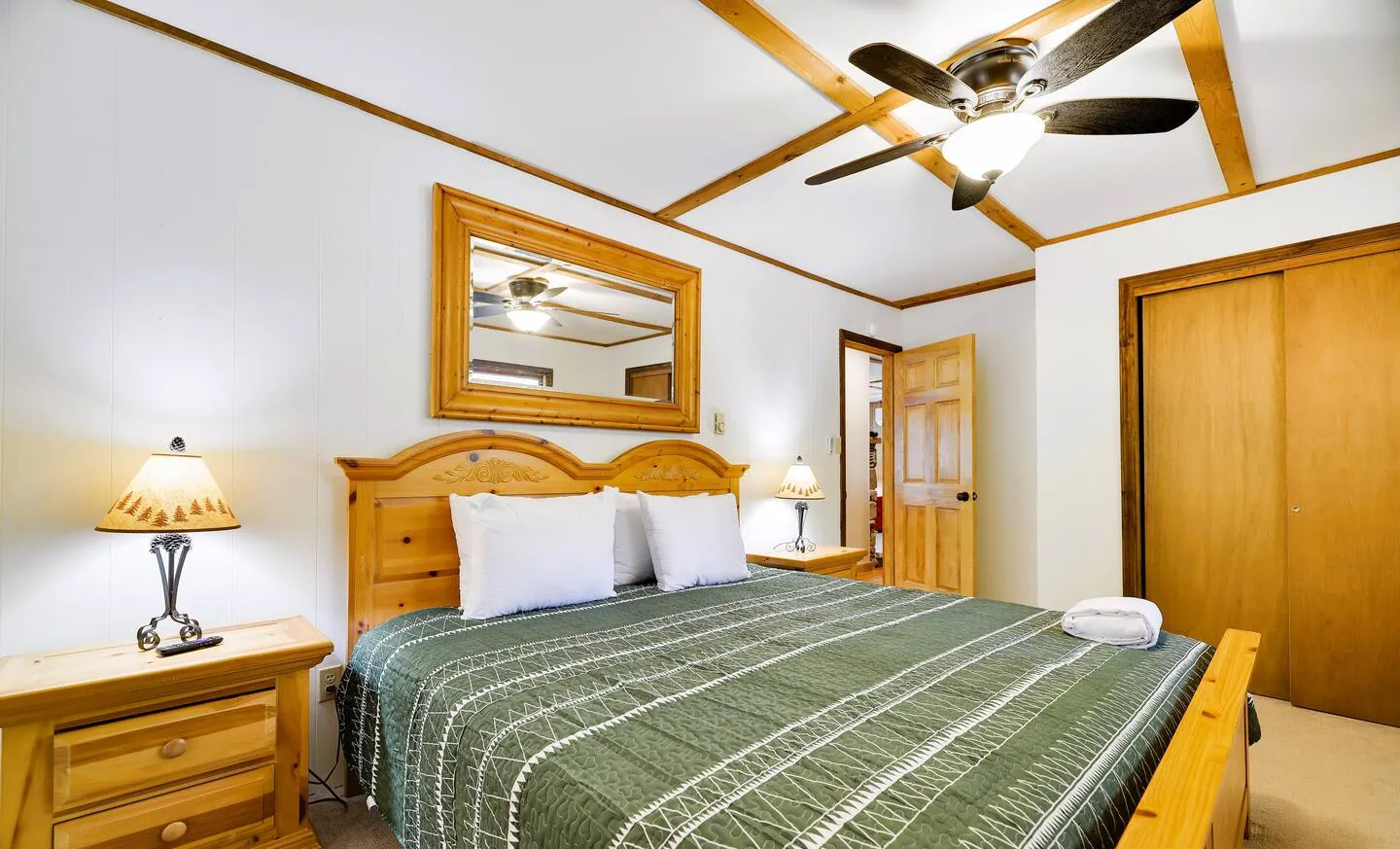 Downstairs king bedroom with pine bed, green quilt and ceiling fan at RedHawk Chalet