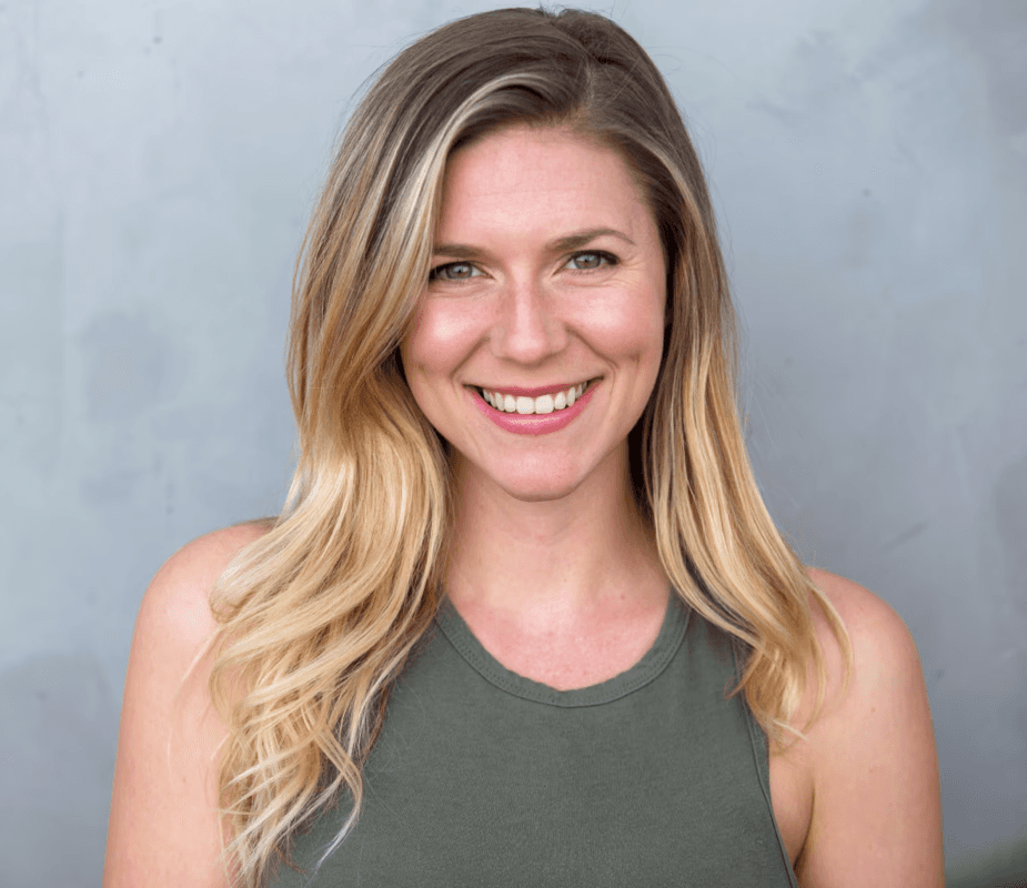Young woman with wavy hair looking away, green building background.
