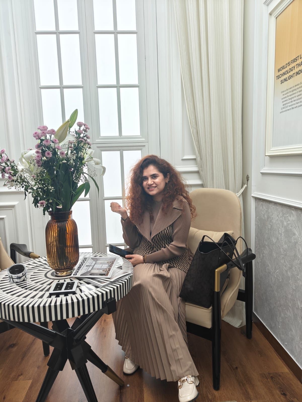 Smiling female therapist with short gray hair, wearing a brown top and a purple shawl, surrounded by a cozy background.