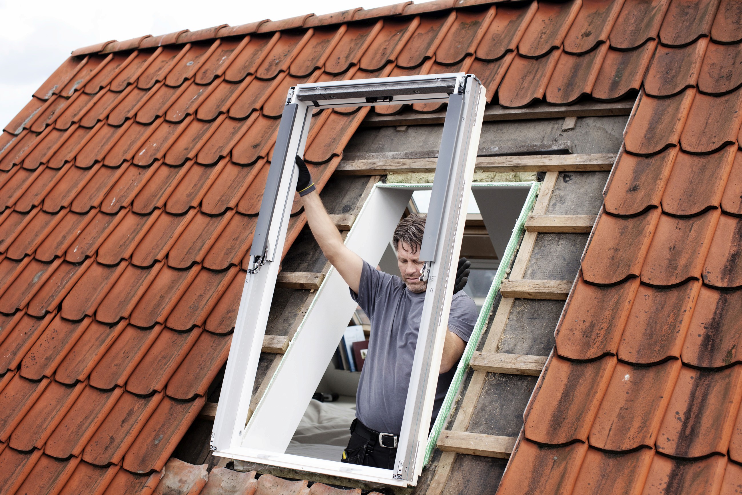 Arbeiter, der ein Dachfenster auf einem Ziegeldach einbaut.