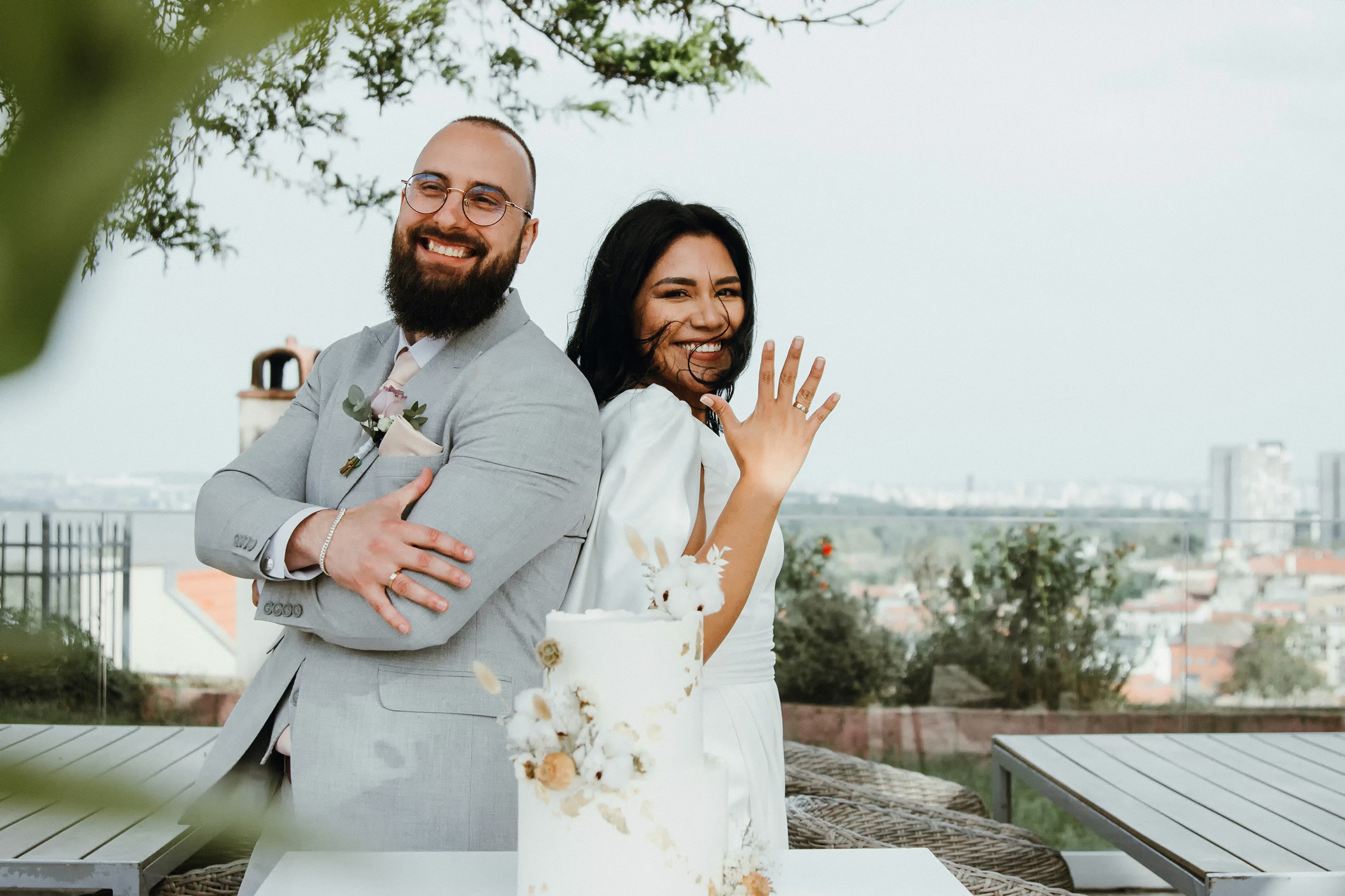 A joyful couple in formal attire stands back-to-back outdoors.