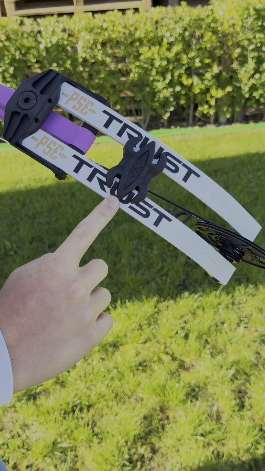 Detail of a PSE TRUST bow; a hand points to a component.