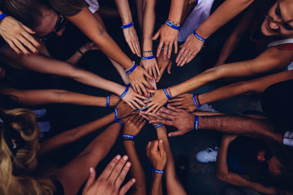 Diverse group of hands together in unity with blue wristbands.