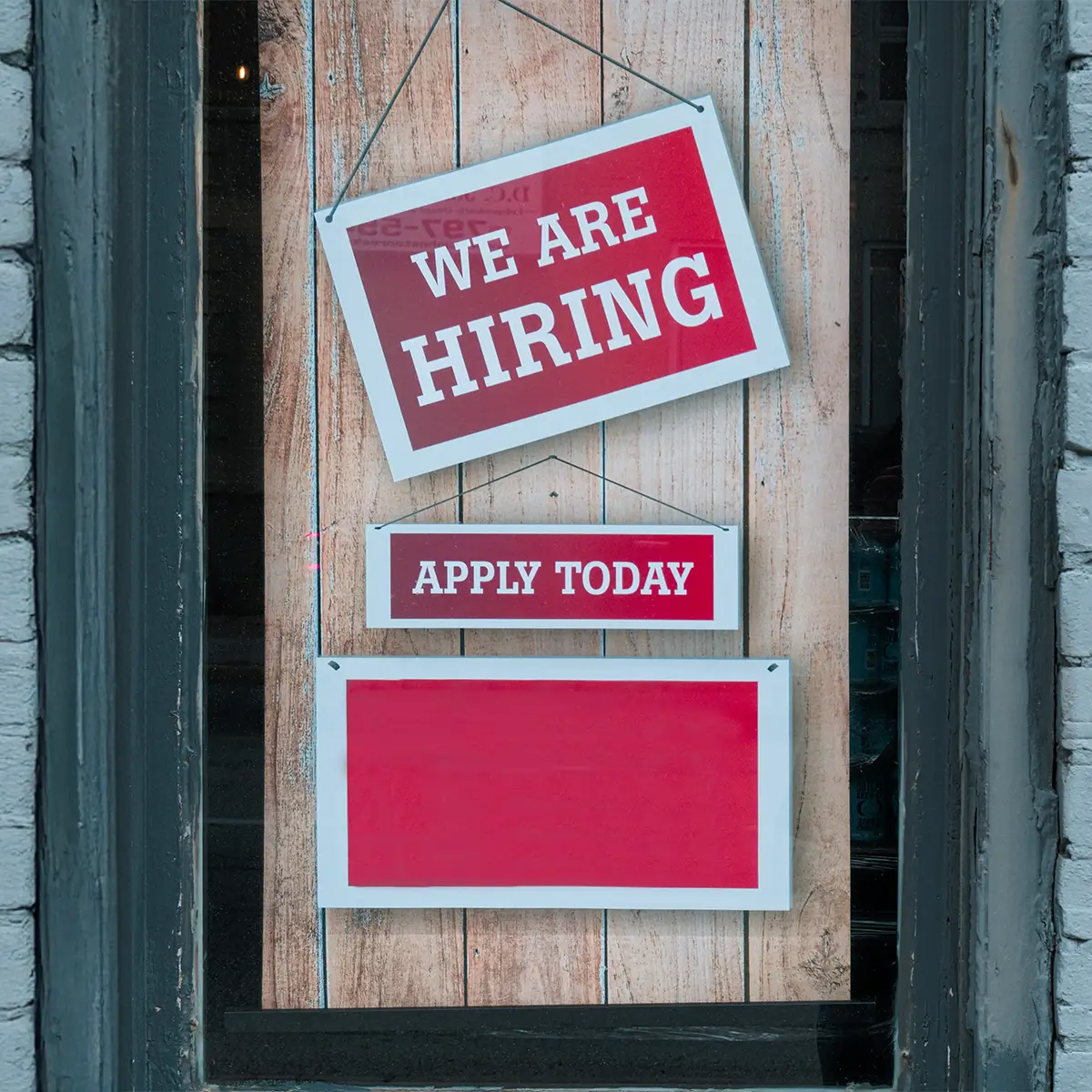 image of signs in a window depecting "we are hiring" and "apply today"