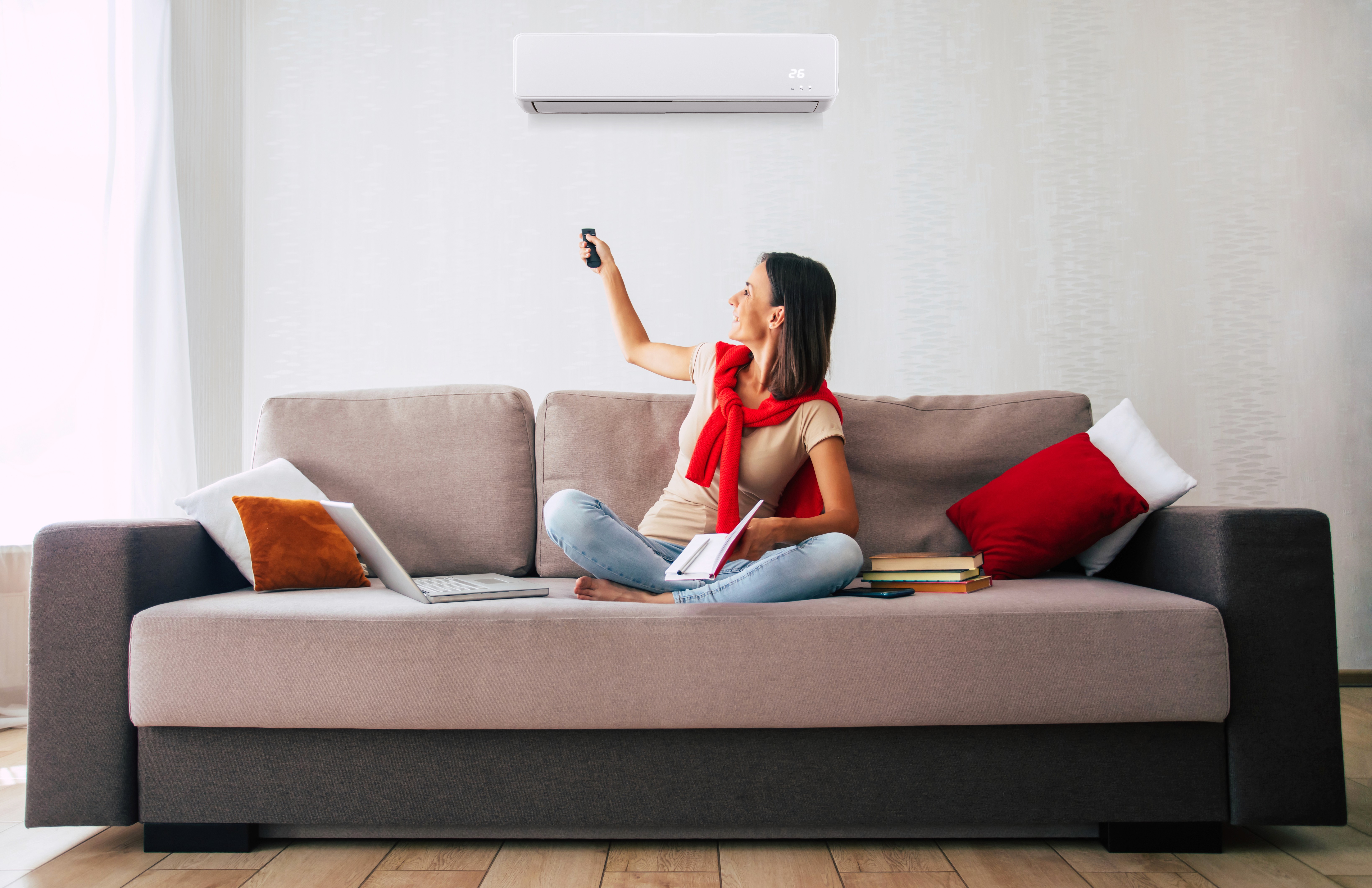 Woman sitting on a couch and turning on AC with remote