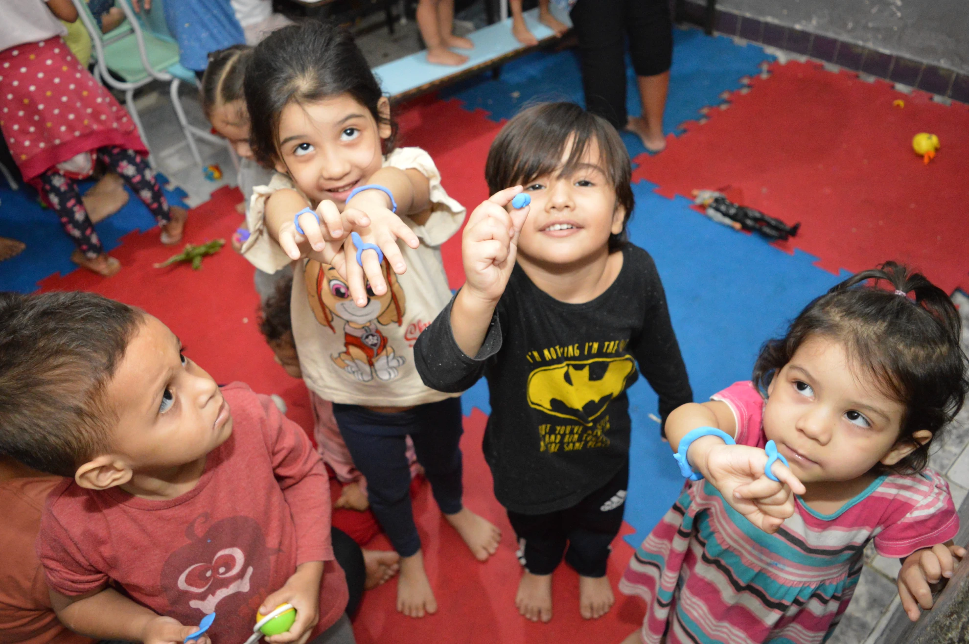 Crianças sorrindo e mostrando trabalhos manuais com papel, em ambiente alegre e acolhedor.