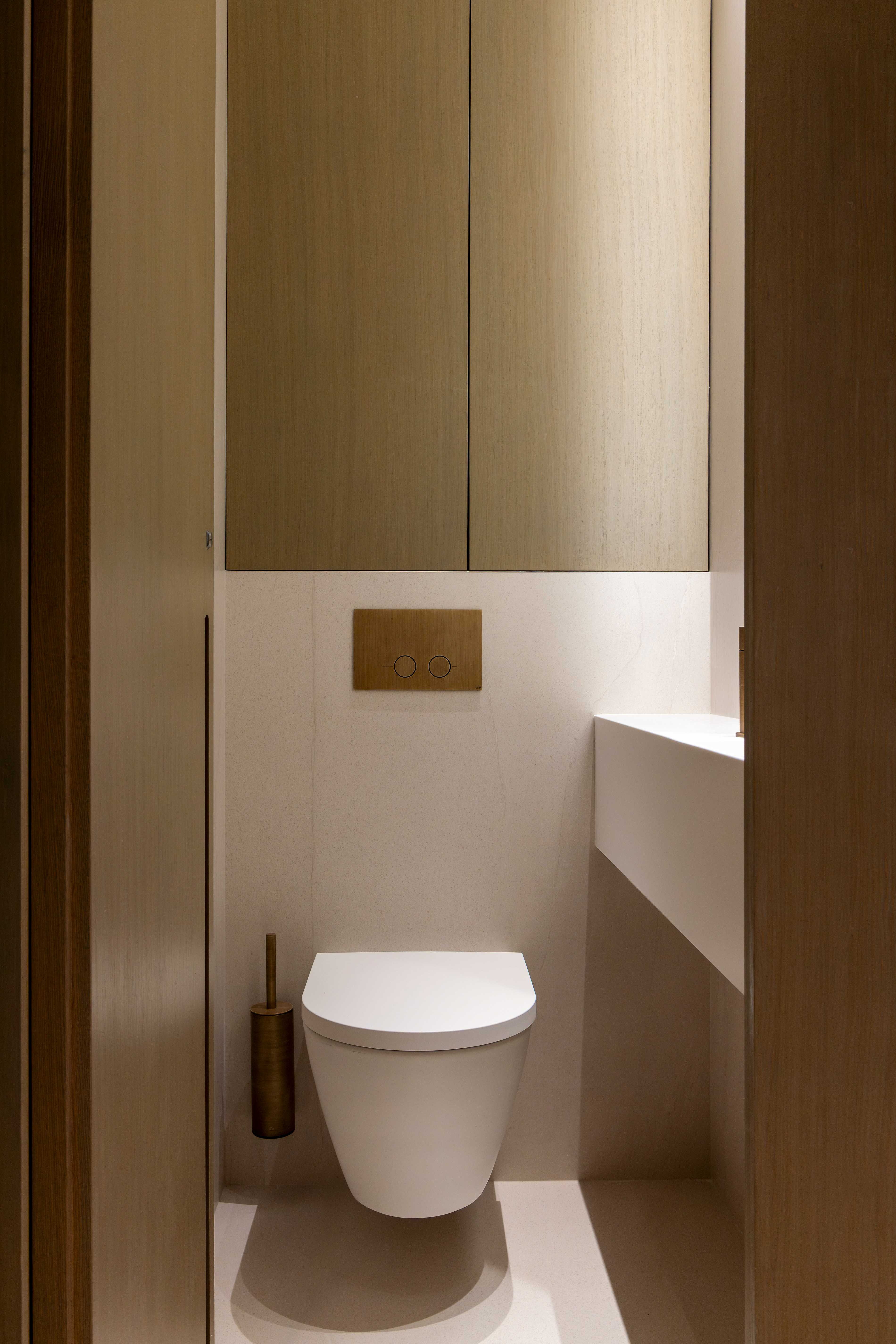 Toilettes suspendues avec plaque de chasse doree, placard bois clair et niche eclairee, tons beiges
