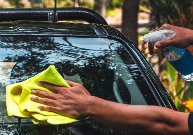 Detailer cleaning a windscreen with a microfibre cloth and spray