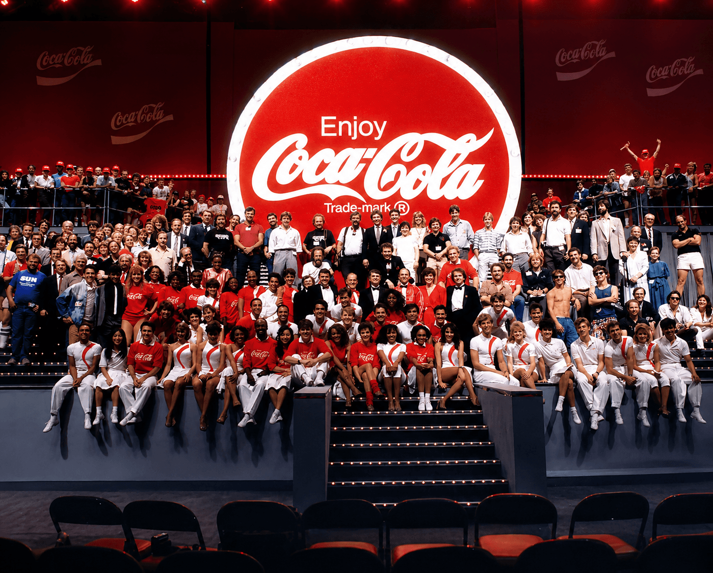 Corporate Magic team and performers gathered onstage beneath a large Coca-Cola sign during the 1986 Coca-Cola Centennial celebration.